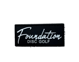 Black patch with 'Foundation Disc Golf' text on a textured surface